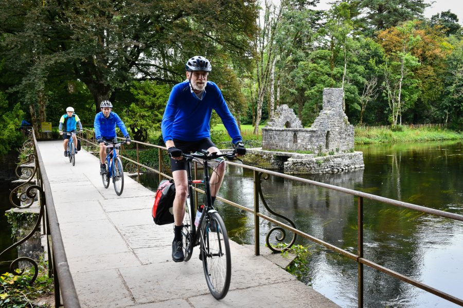 Cyclists cross the River Cong, passing an ancient Irish monastery's fisherman's hut